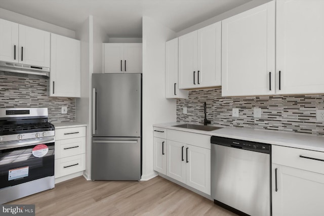 kitchen featuring stainless steel appliances, a sink, under cabinet range hood, light countertops, and light wood-type flooring