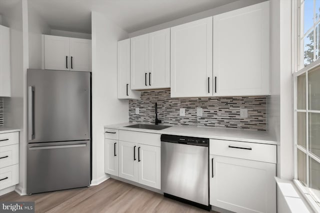 kitchen featuring stainless steel appliances, a sink, light wood-style floors, and decorative backsplash
