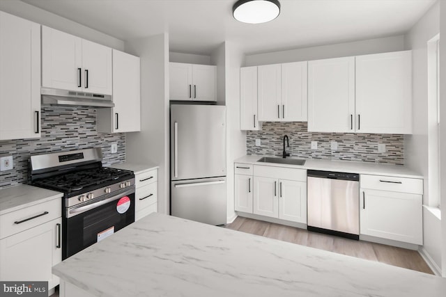 kitchen featuring stainless steel appliances, under cabinet range hood, a sink, white cabinets, and tasteful backsplash