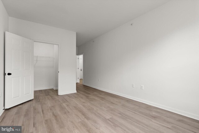 unfurnished bedroom featuring light wood-style floors, a closet, baseboards, and a spacious closet