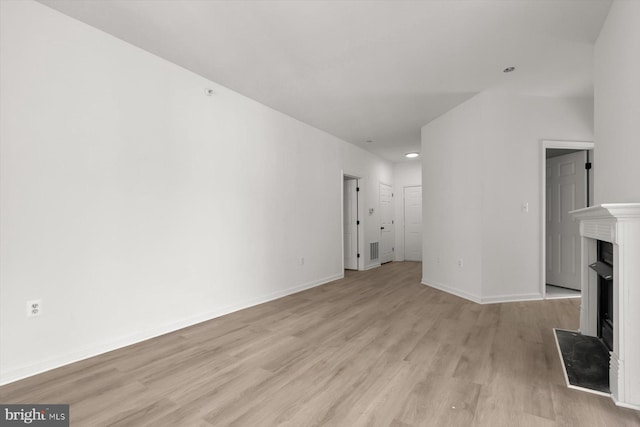 unfurnished living room with light wood-style flooring, a fireplace with raised hearth, and baseboards