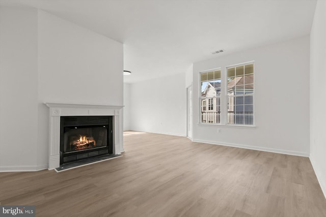 unfurnished living room with wood finished floors, a warm lit fireplace, and baseboards