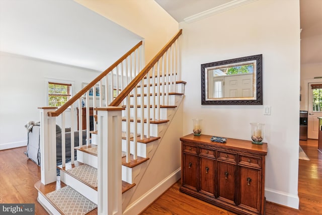 stairs with wood finished floors, healthy amount of natural light, baseboards, and ornamental molding
