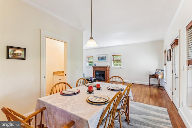 dining space featuring wood finished floors, a glass covered fireplace, ornamental molding, and baseboards
