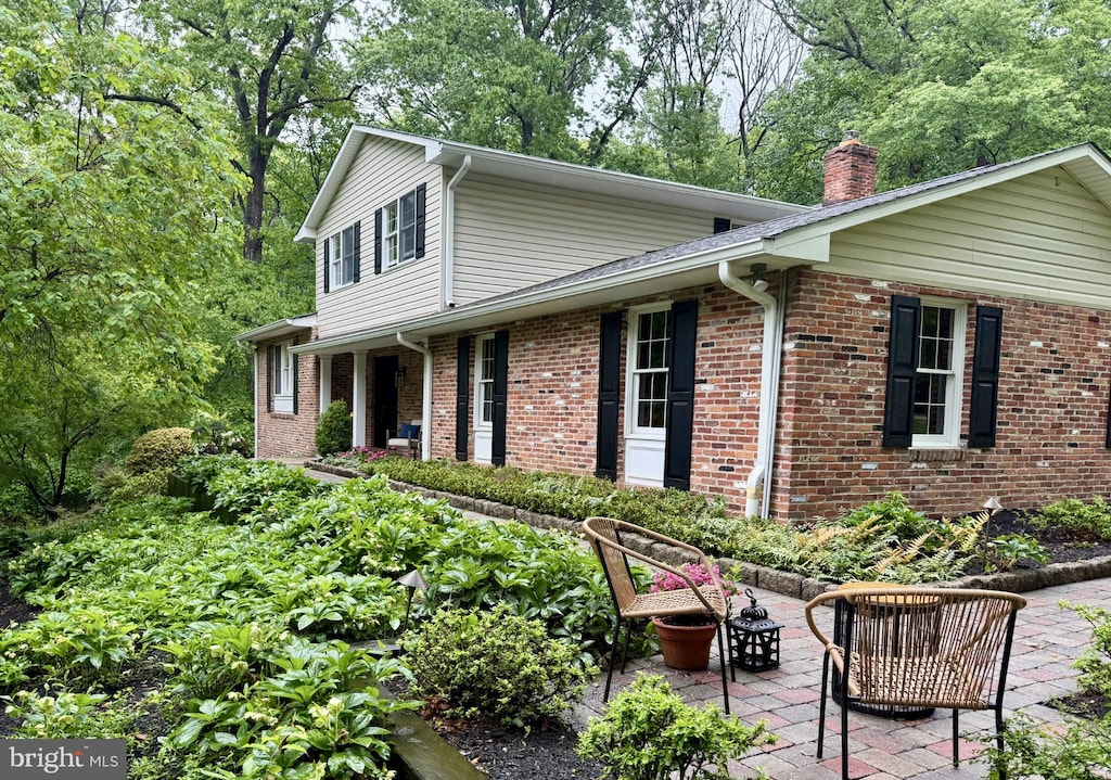 view of front facade featuring a chimney, brick siding, and a patio