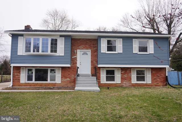 bi-level home with entry steps, brick siding, a front lawn, and a chimney