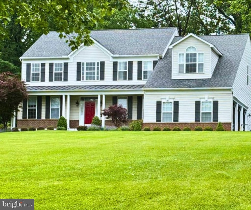 colonial inspired home featuring a front lawn, a porch, a standing seam roof, and roof with shingles