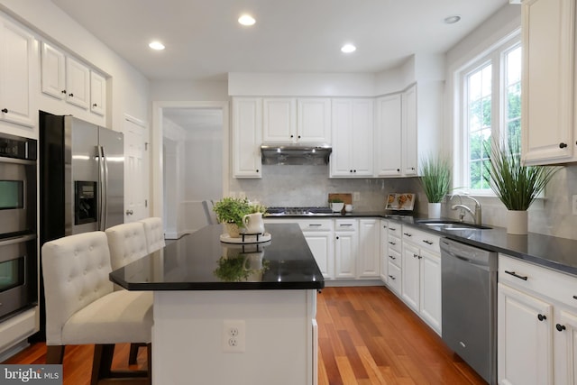 kitchen with appliances with stainless steel finishes, a sink, tasteful backsplash, a kitchen breakfast bar, and dark countertops