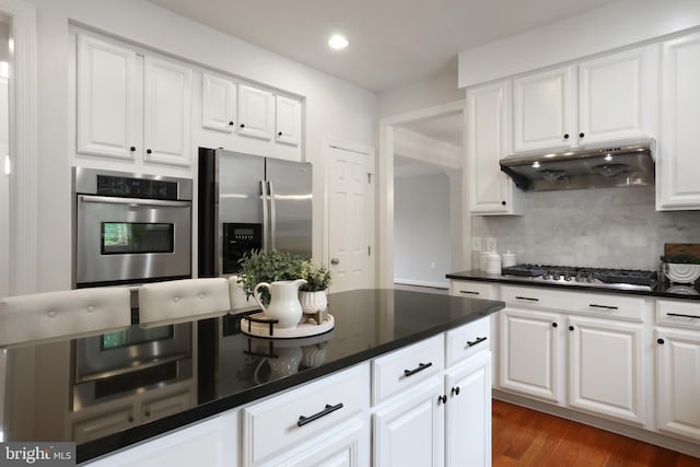 kitchen with stainless steel appliances, under cabinet range hood, dark countertops, white cabinets, and recessed lighting