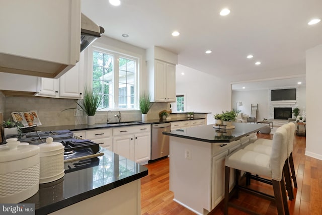 kitchen with stainless steel dishwasher, a sink, dark countertops, light wood-type flooring, and white cabinets