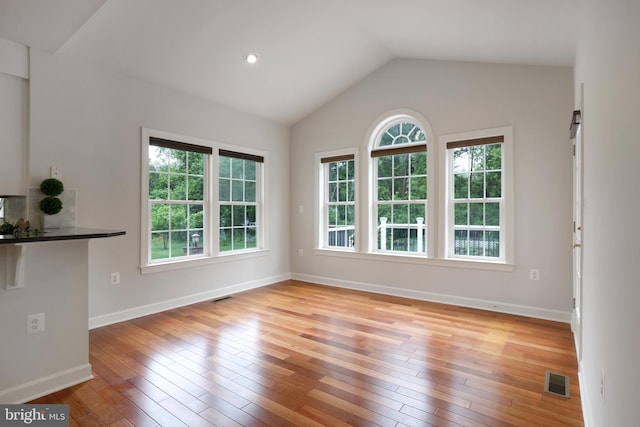 unfurnished living room featuring healthy amount of natural light, light wood-style floors, lofted ceiling, and baseboards