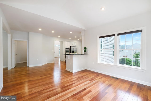 unfurnished living room featuring light wood finished floors, baseboards, lofted ceiling, and recessed lighting