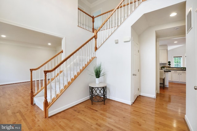 staircase featuring wood finished floors, recessed lighting, baseboards, and a high ceiling