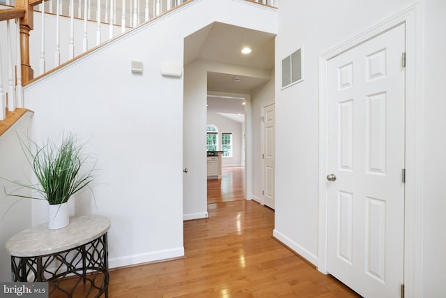 hall featuring light wood-style flooring, baseboards, stairs, and recessed lighting