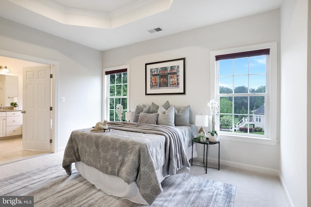 bedroom with a tray ceiling, baseboards, crown molding, connected bathroom, and light colored carpet
