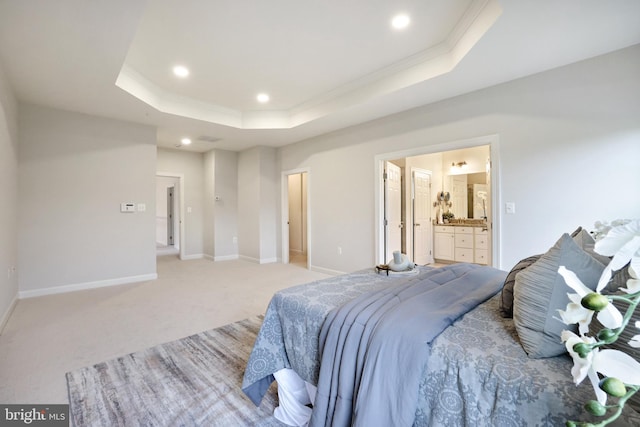 bedroom with a raised ceiling, recessed lighting, light carpet, baseboards, and ensuite bath