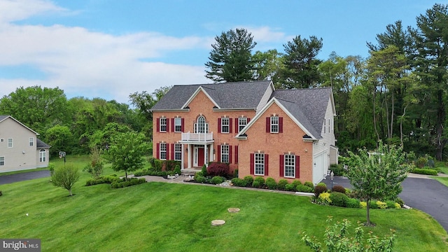 colonial house with a front yard, a balcony, brick siding, and asphalt driveway