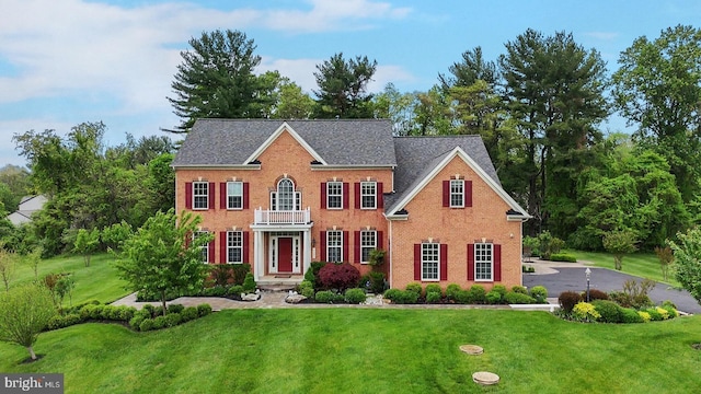 georgian-style home featuring a front yard, a balcony, and brick siding