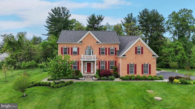 colonial house featuring a front yard, a balcony, and brick siding