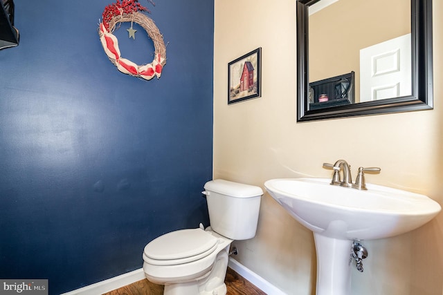 bathroom with baseboards, toilet, wood finished floors, and a sink