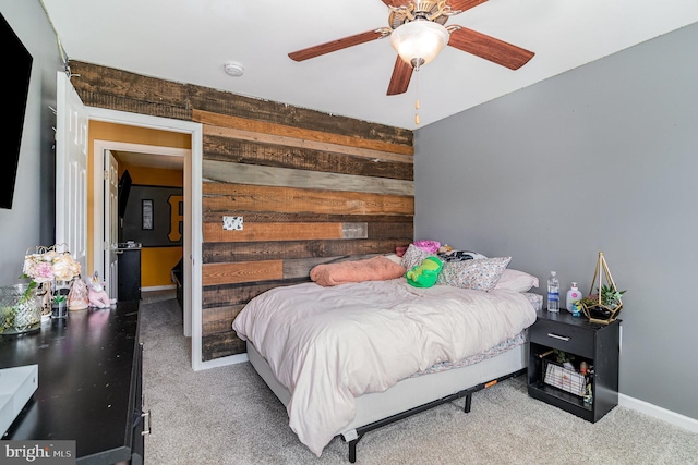 carpeted bedroom with wooden walls, a ceiling fan, and baseboards