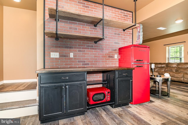 kitchen with wood finished floors, freestanding refrigerator, and dark cabinetry