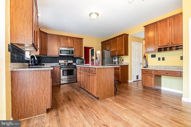 kitchen with appliances with stainless steel finishes, wood finished floors, decorative backsplash, and brown cabinets