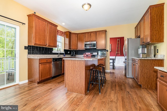 kitchen featuring stainless steel appliances, wood finished floors, brown cabinetry, and plenty of natural light
