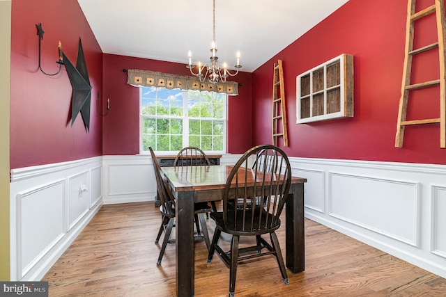 dining area featuring a chandelier, wainscoting, wood finished floors, and a decorative wall