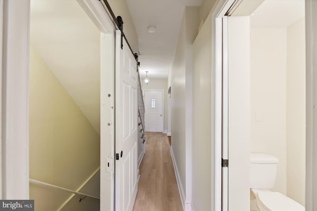 corridor with a barn door, light wood-style flooring, and baseboards