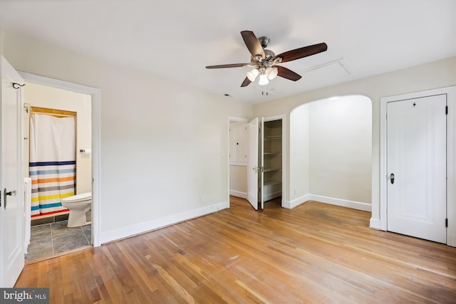 unfurnished bedroom featuring baseboards, arched walkways, two closets, and wood finished floors