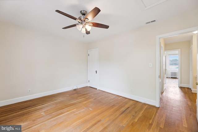 empty room with radiator, a ceiling fan, light wood finished floors, and baseboards