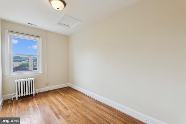 unfurnished room featuring radiator, baseboards, light wood-style flooring, and attic access