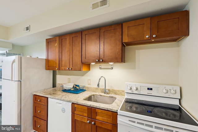 kitchen with white appliances, a sink, brown cabinets, and light stone countertops
