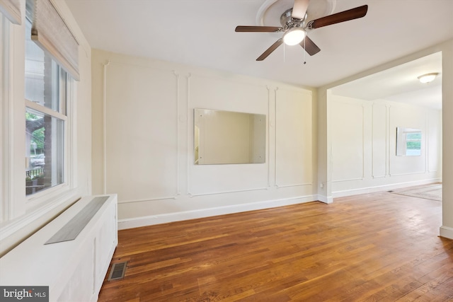spare room featuring plenty of natural light, light wood-style floors, a decorative wall, and ceiling fan