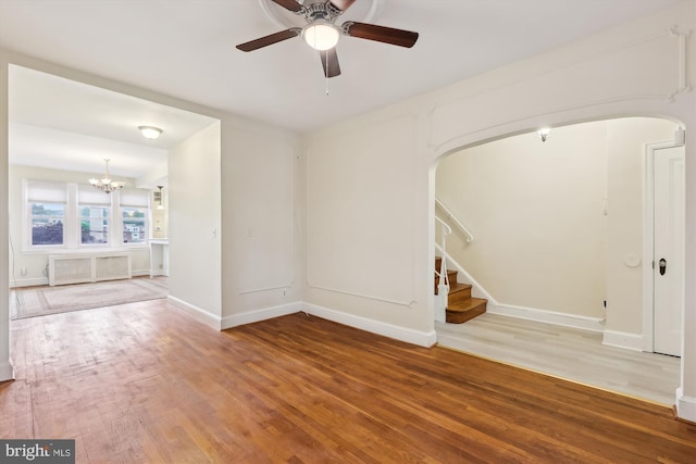 unfurnished room with wood finished floors, arched walkways, a chandelier, stairs, and ceiling fan