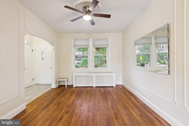 spare room with healthy amount of natural light, wood finished floors, a ceiling fan, and radiator heating unit