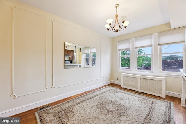 unfurnished dining area with a chandelier, wood finished floors, and baseboards