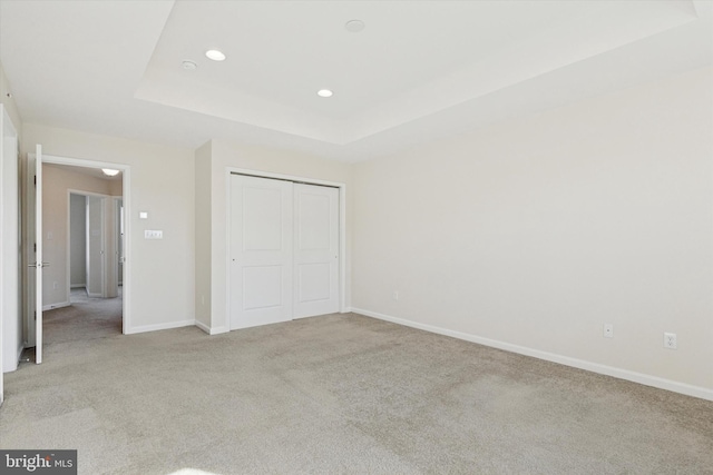 unfurnished bedroom featuring light carpet, a closet, recessed lighting, a tray ceiling, and baseboards