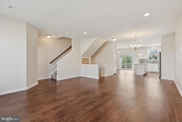 unfurnished living room with a chandelier, dark wood finished floors, recessed lighting, stairs, and baseboards