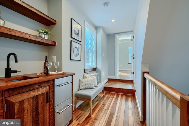 corridor with a sink, light wood-type flooring, recessed lighting, and baseboards