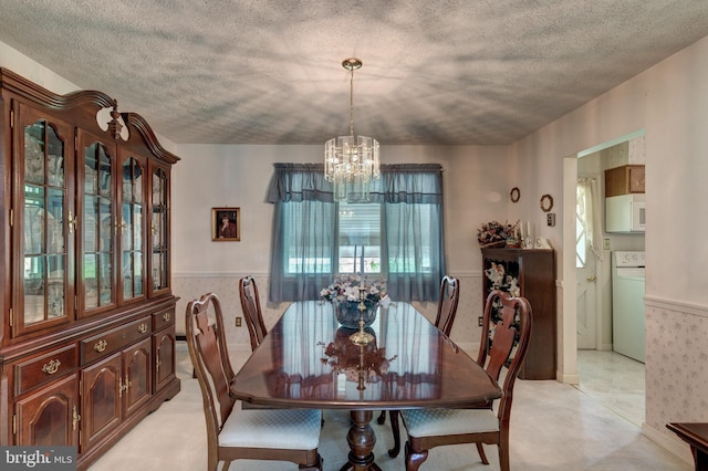dining area featuring a chandelier, plenty of natural light, a textured ceiling, washer / clothes dryer, and wainscoting
