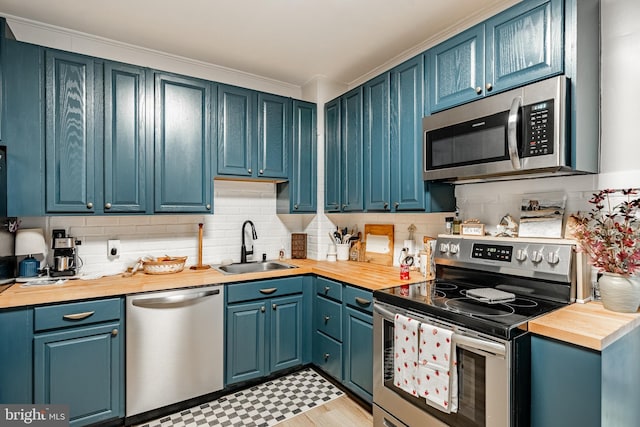 kitchen with appliances with stainless steel finishes, butcher block counters, a sink, tasteful backsplash, and crown molding