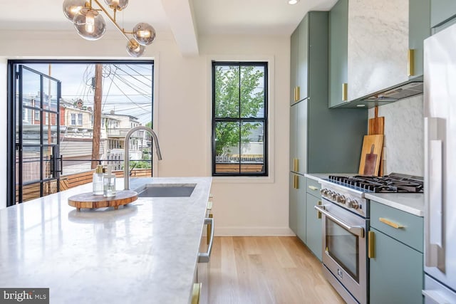 kitchen with high end stove, a sink, a chandelier, green cabinetry, and light wood-style floors