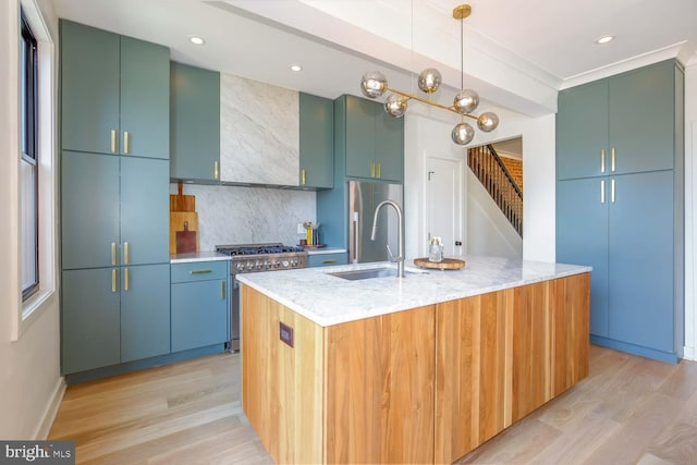 kitchen with high end appliances, a sink, tasteful backsplash, light wood-style floors, and an island with sink