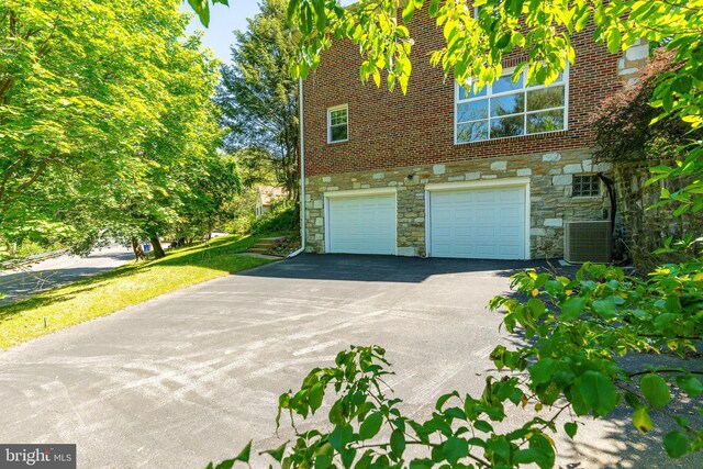 1128 Coventry Rd, Cheltenham, PA 19012 - view of side of property with stone siding, asphalt driveway, an attached garage, and central AC unit