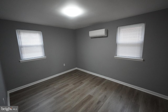 empty room with a wall mounted AC, wood finished floors, and baseboards