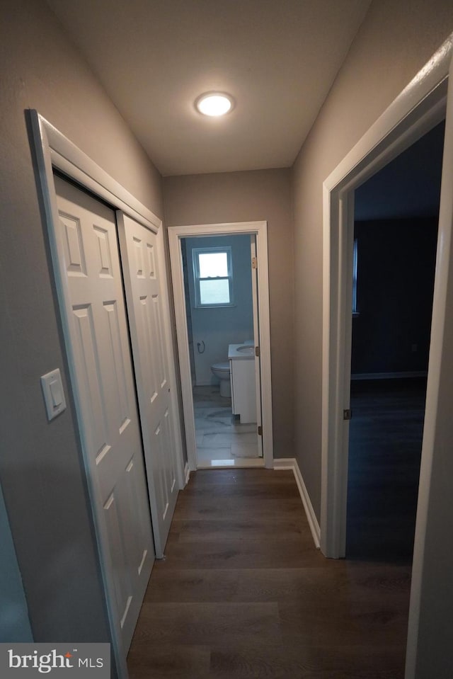 corridor featuring dark wood-type flooring and baseboards