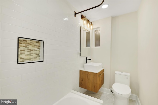 bathroom featuring toilet, vanity, a tub to relax in, and baseboards