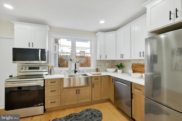 kitchen with appliances with stainless steel finishes, a sink, light countertops, backsplash, and light wood-style floors